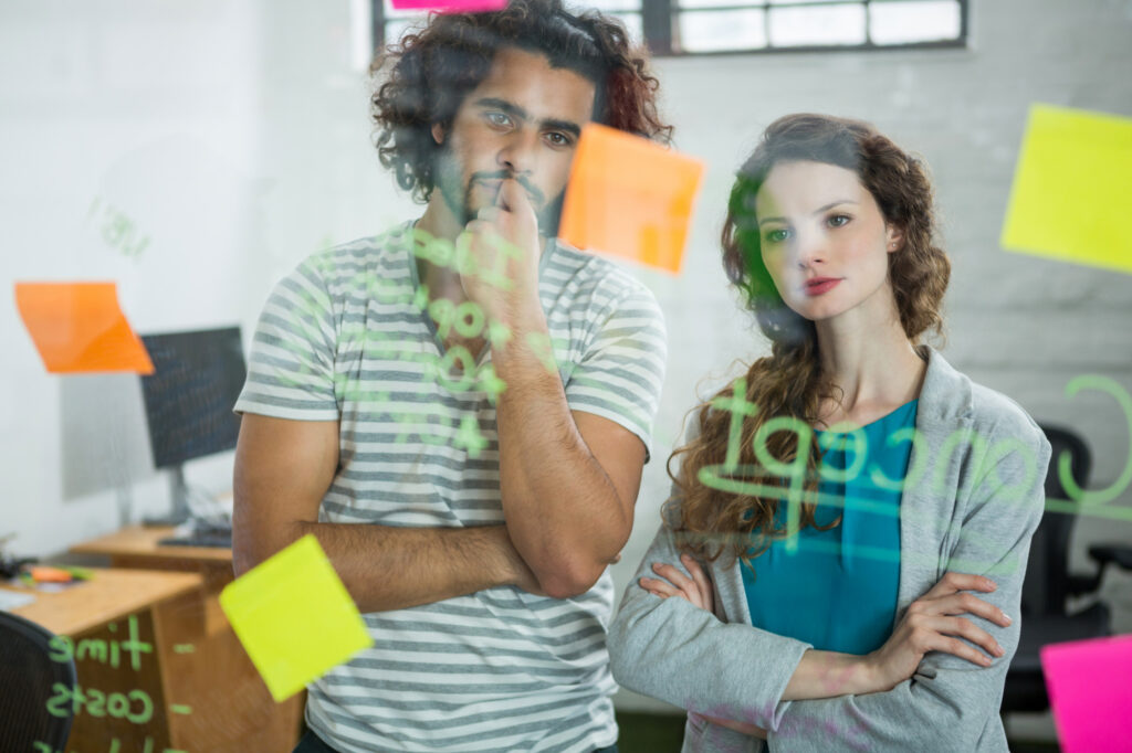 Equipo de trabajo analizando ideas en pizarra de cristal con notas adhesivas