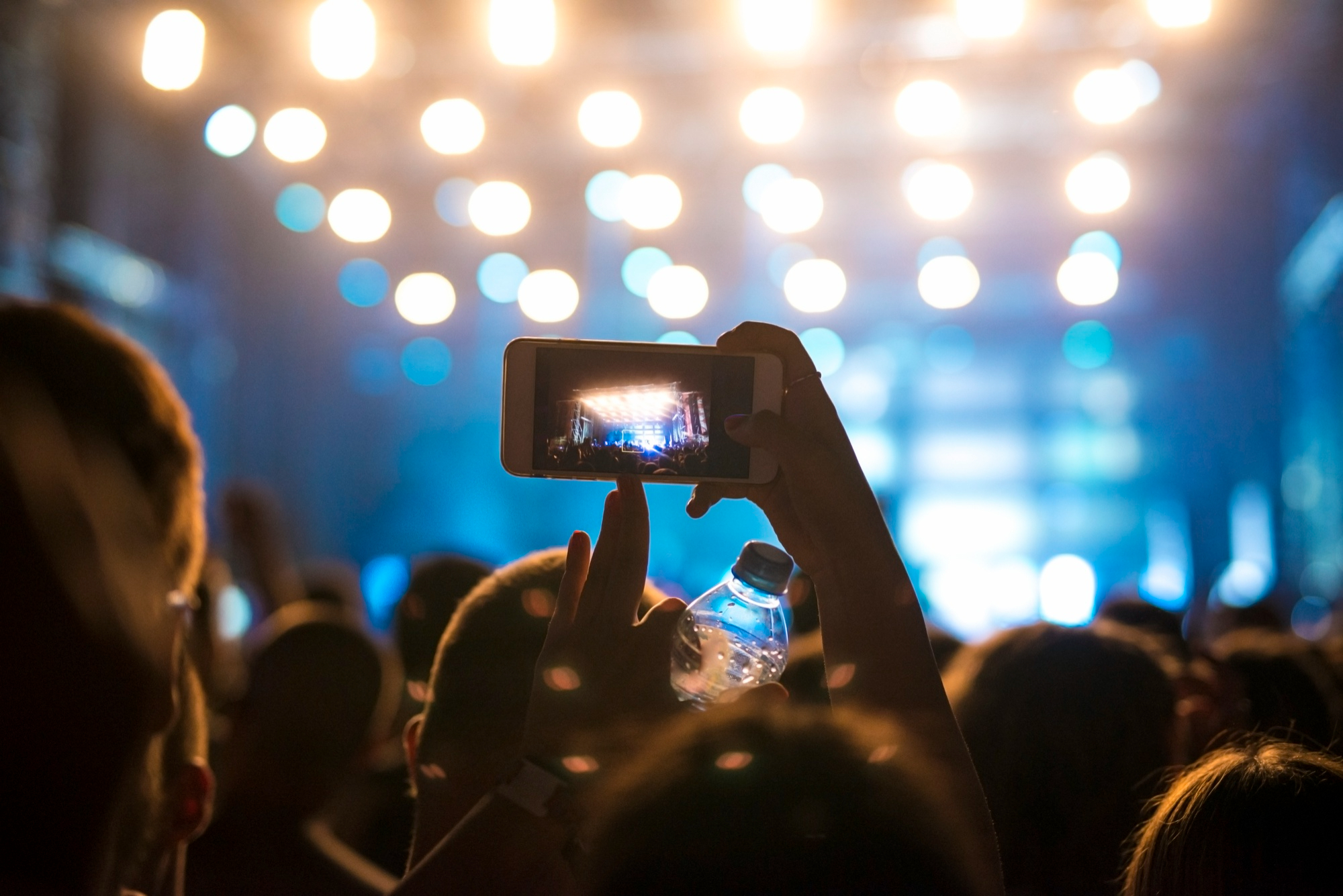 Mujer en la multitud tomando una foto del escenario en un festival de música