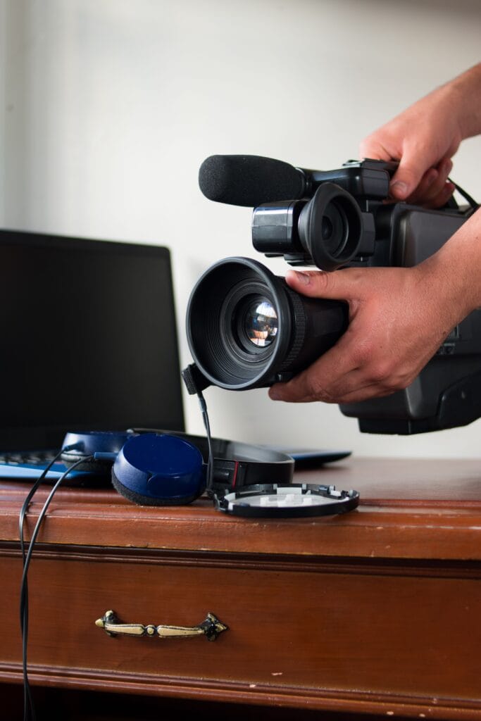 Primer plano de una cámara profesional sostenida sobre un escritorio de madera con un portátil en el fondo