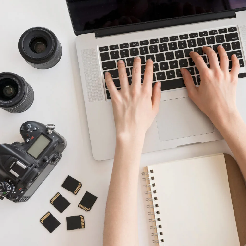 Fotógrafo trabajando en laptop con cámara profesional y tarjetas de memoria