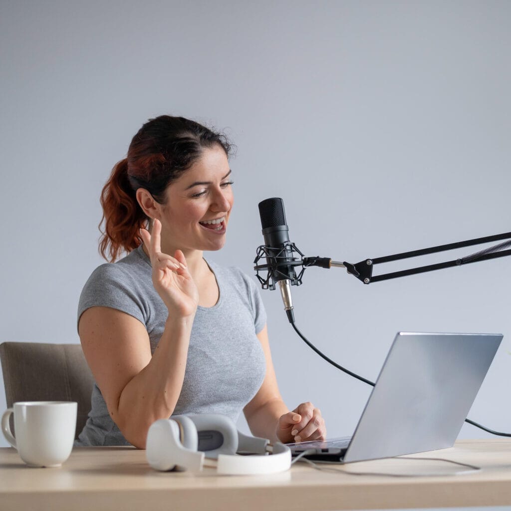 Mujer grabando pódcast con micrófono y laptop en casa